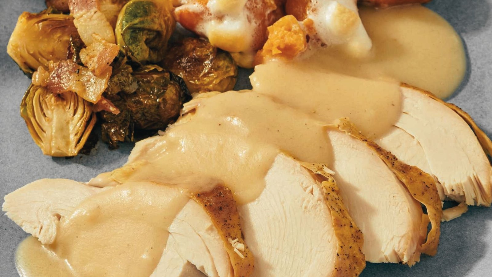 A Roasted turkey served with sautéed Brussels sprouts, rich gravy, and bread on a plate