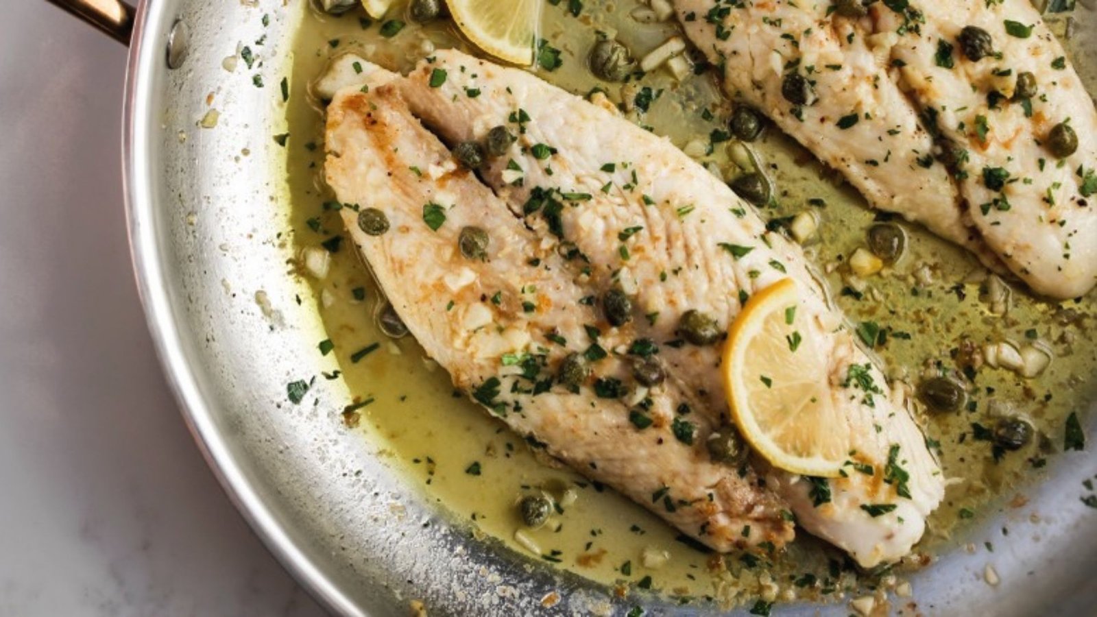 Two swai fish fillets cooking in a pan, garnished with fresh lemon slices for flavor enhancement.