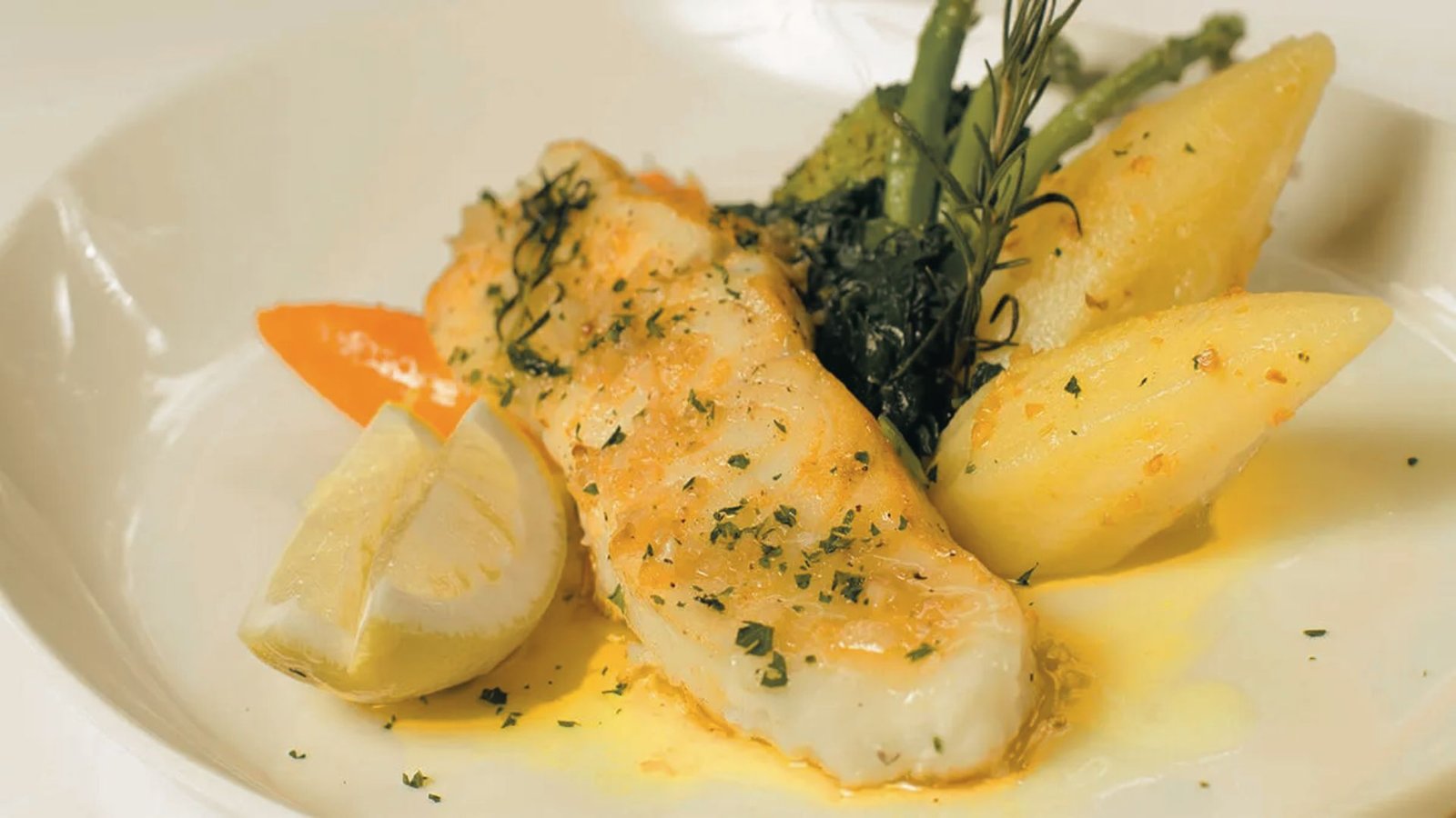 A plate featuring Lemon Butter Baked Corvina fish, alongside potatoes and asparagus, beautifully arranged for a meal.