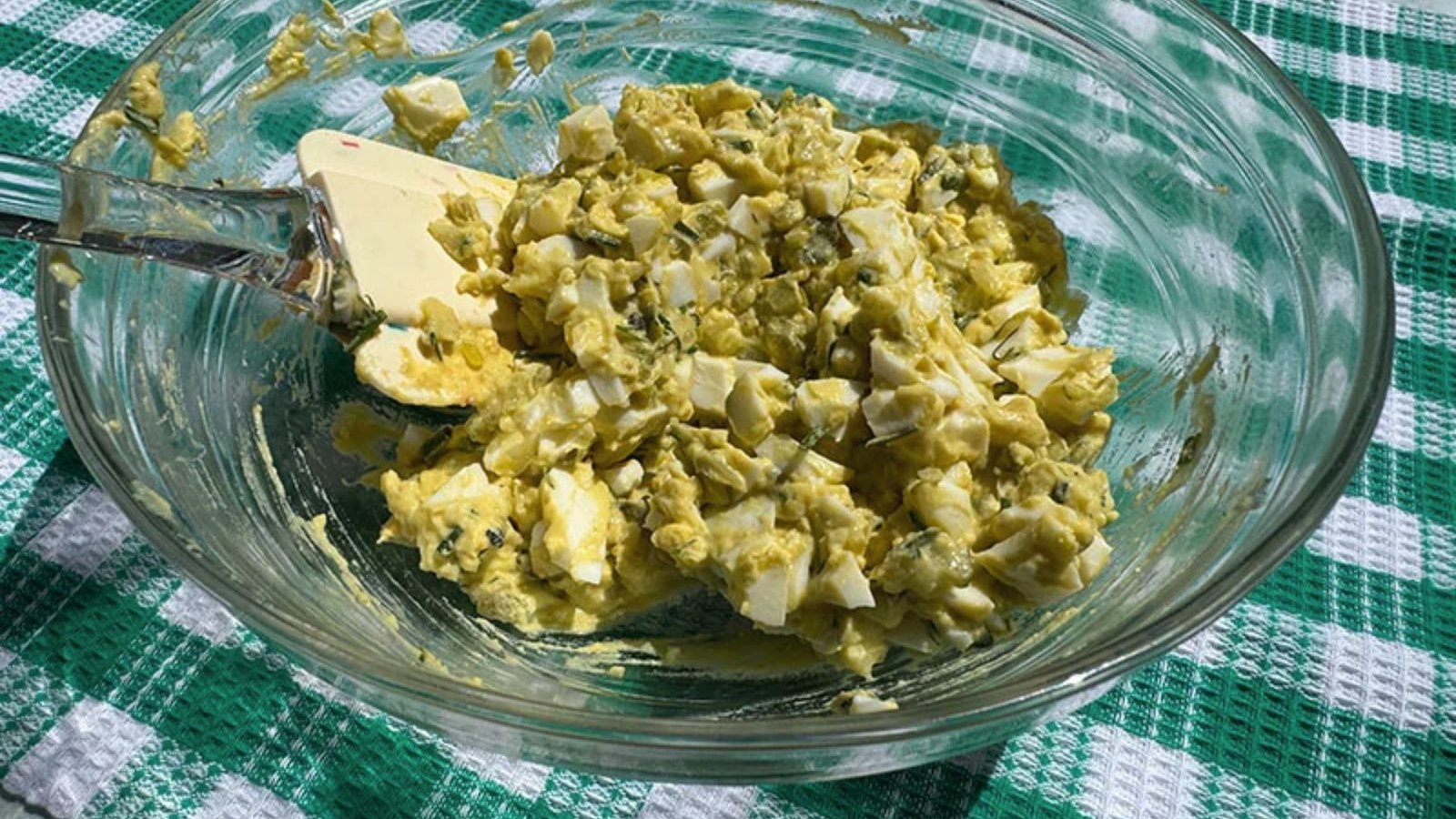A bowl of egg and adding tangy pickles to it.