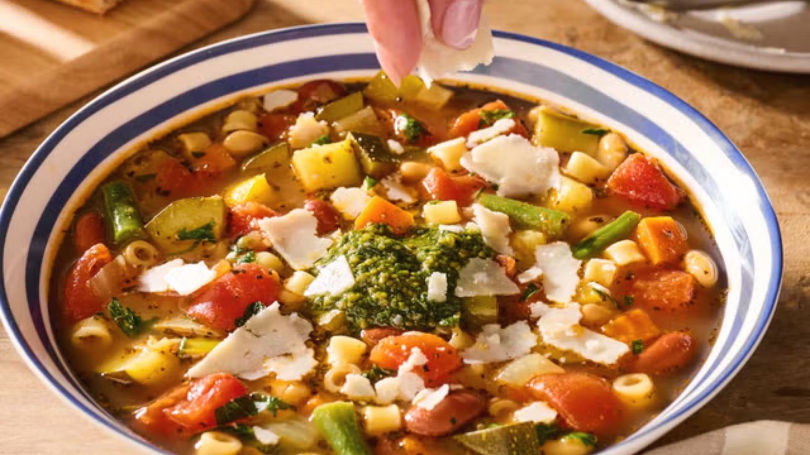 A bowl of hearty minestrone soup filled with pasta, vegetables, and topped with cheese.