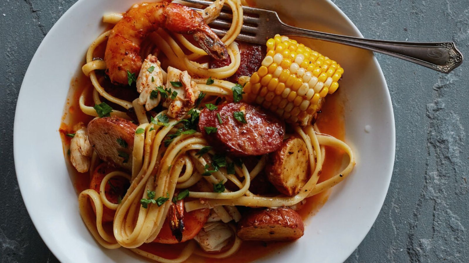 A serving of pasta with shrimp and crab, with a fork placed on the side of the plate.