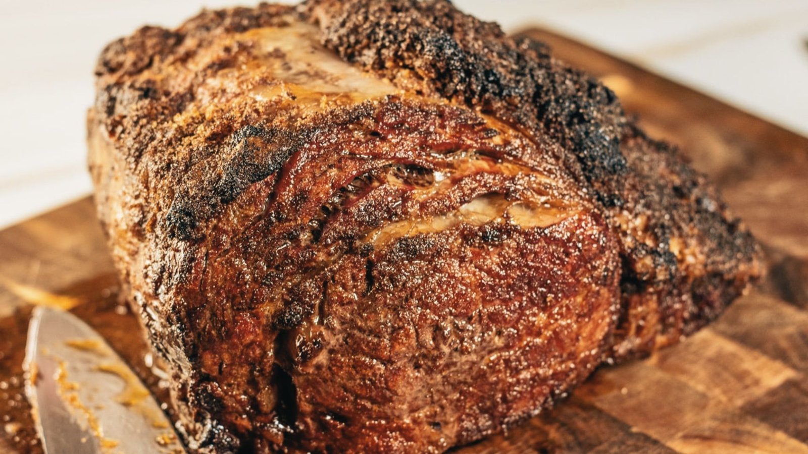 A large roast on a wooden cutting board with a sharp knife beside it, showcasing a classic oven roast preparation.