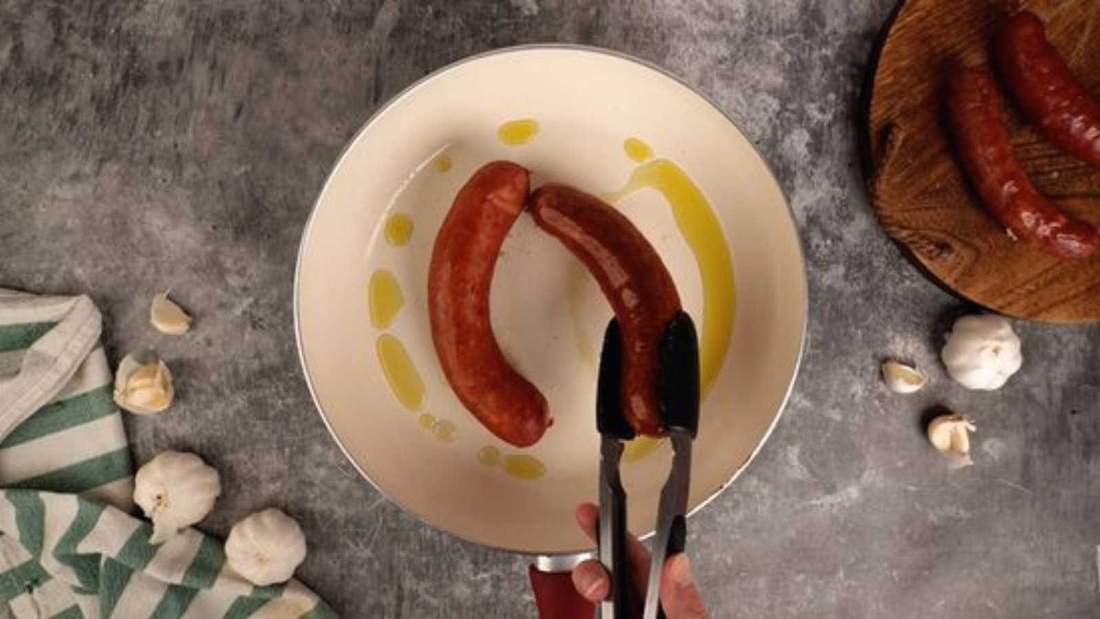 A person holds a frying pan with two sausages, illustrating a step in a deer sausage recipe guide.