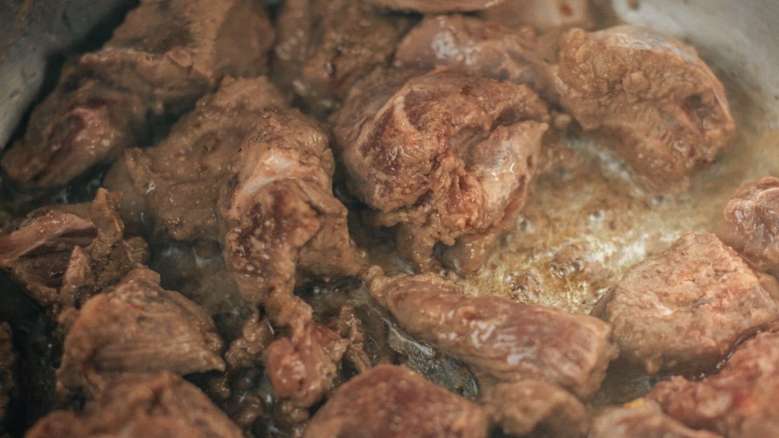 Close-up view of meat sizzling in a pan, illustrating the first step of searing for stew preparation.