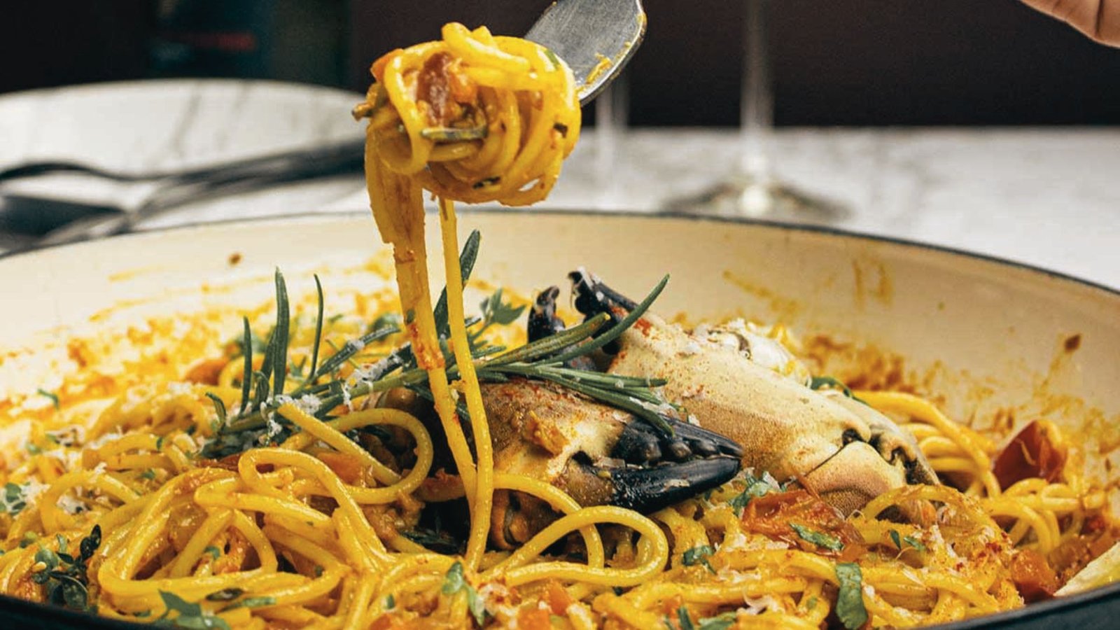 A person holds a spoon over a delicious crab and shrimp pasta dish, contemplating which recipe to choose.