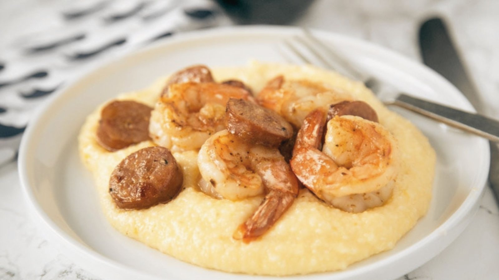 A bowl of shrimp and grits topped with sausage, showcasing a delicious Southern dish.