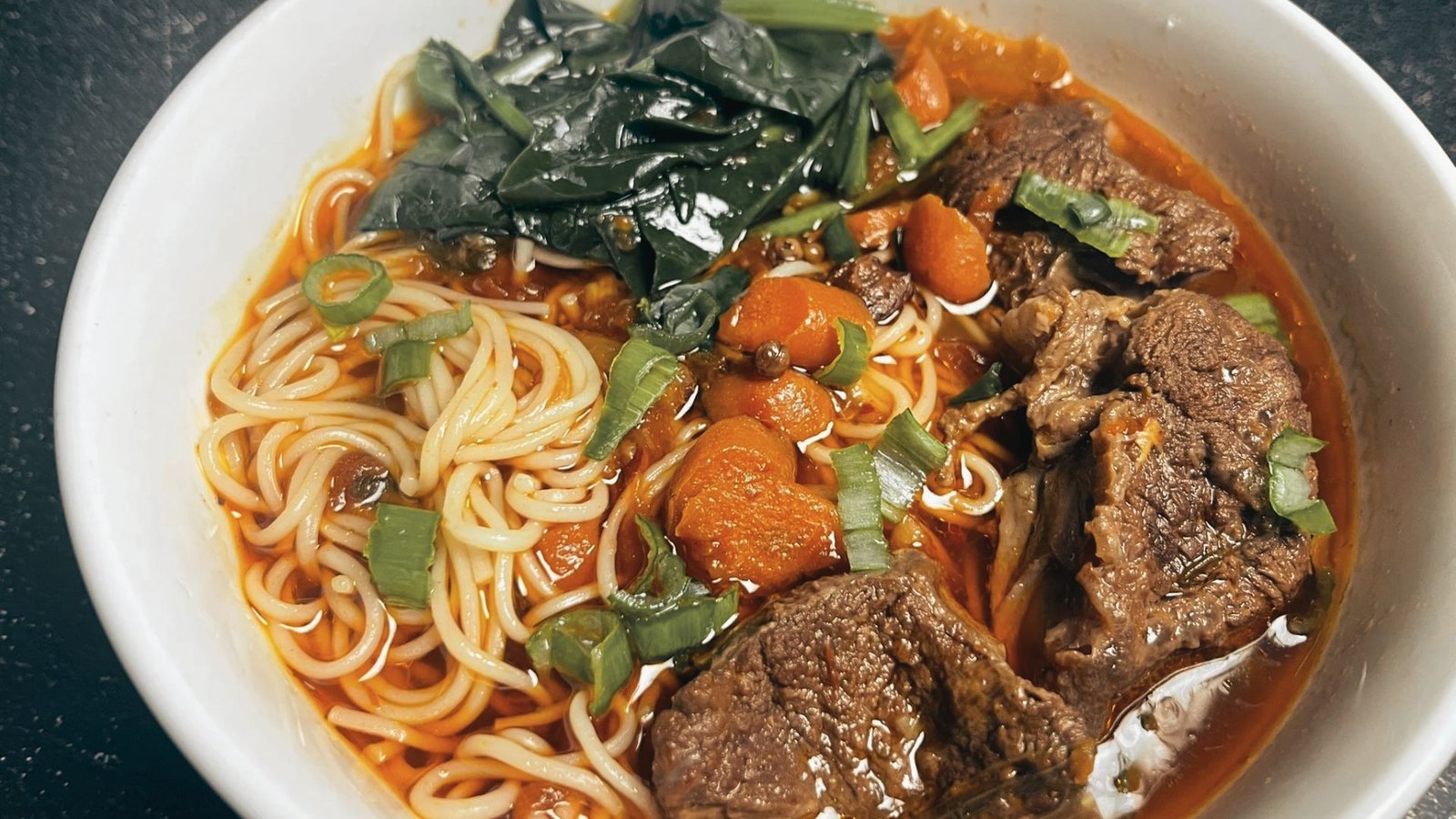 A bowl of beef noodle soup filled with tender meat, colorful vegetables, and steaming noodles.