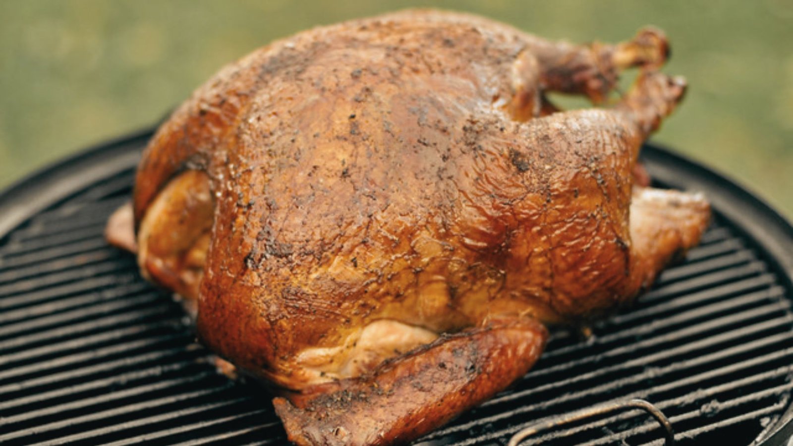A grilled roasted turkey with a vibrant green background, highlighting a recipe for Cajun smoked turkey rub with spice.
