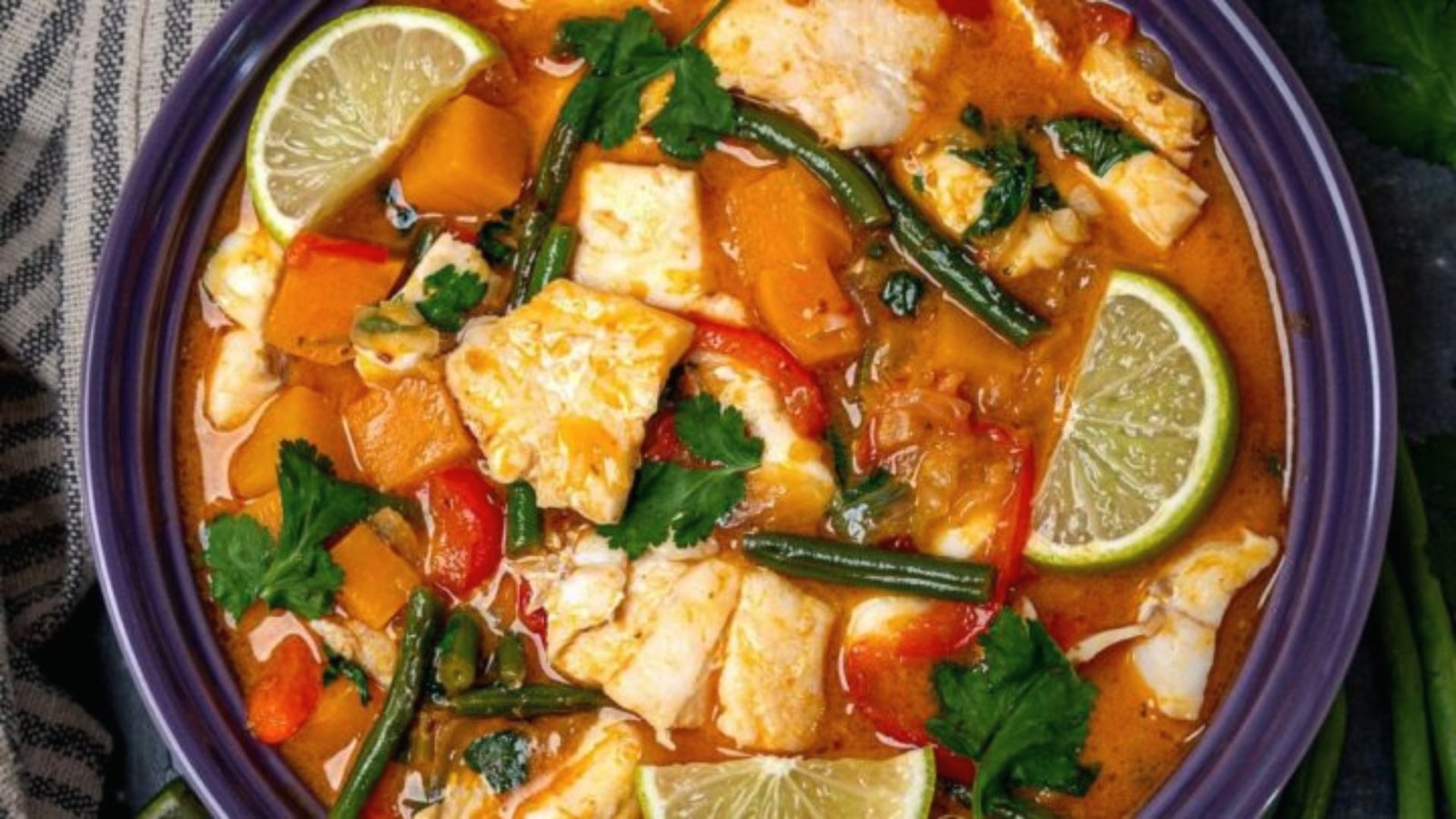 A vibrant bowl of homemade Thai fish stew with assorted vegetables and a slice of lime for garnish.