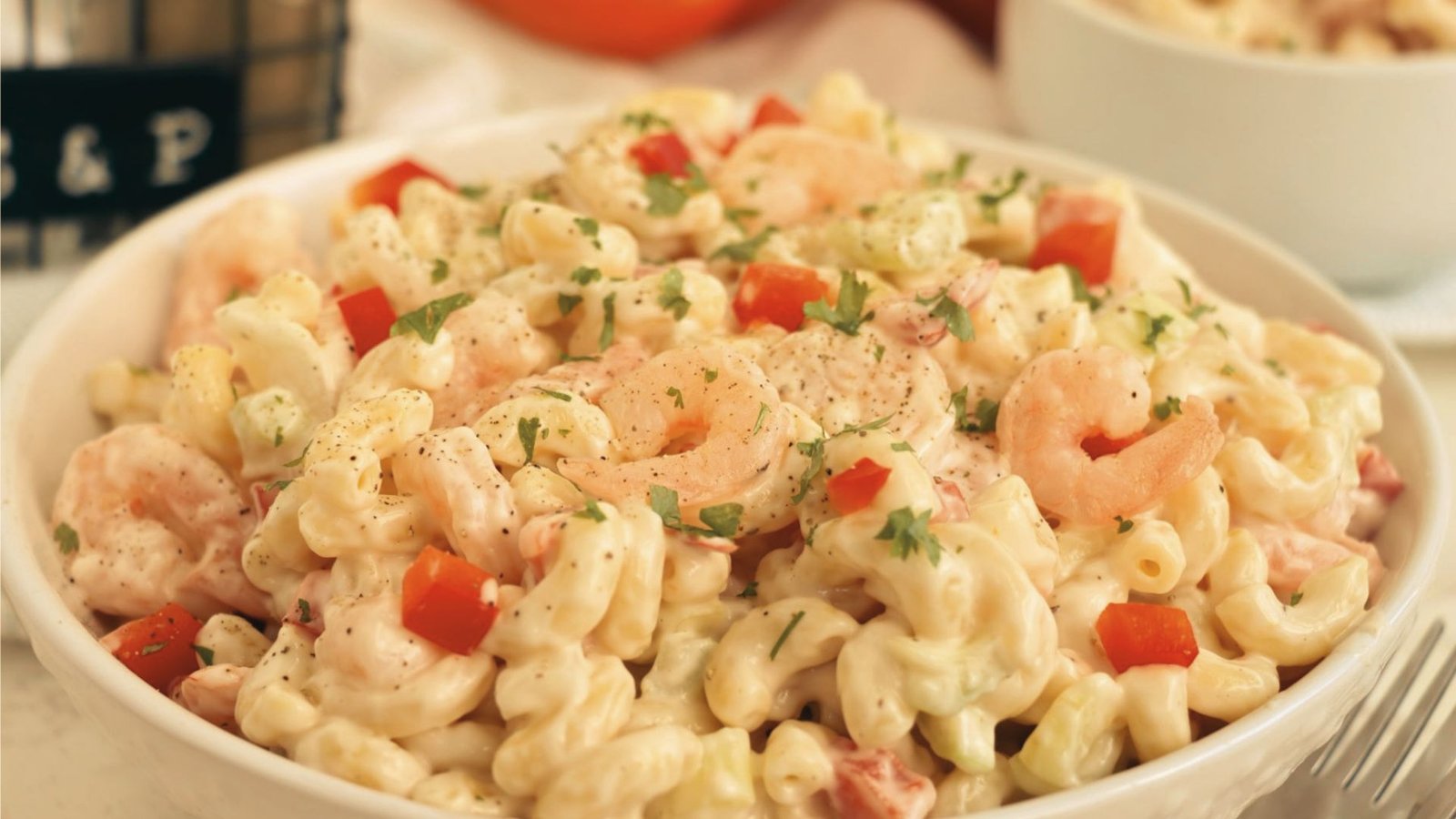 A colorful bowl of shrimp pasta salad with fresh tomatoes, ideal for summer gatherings and cookouts.