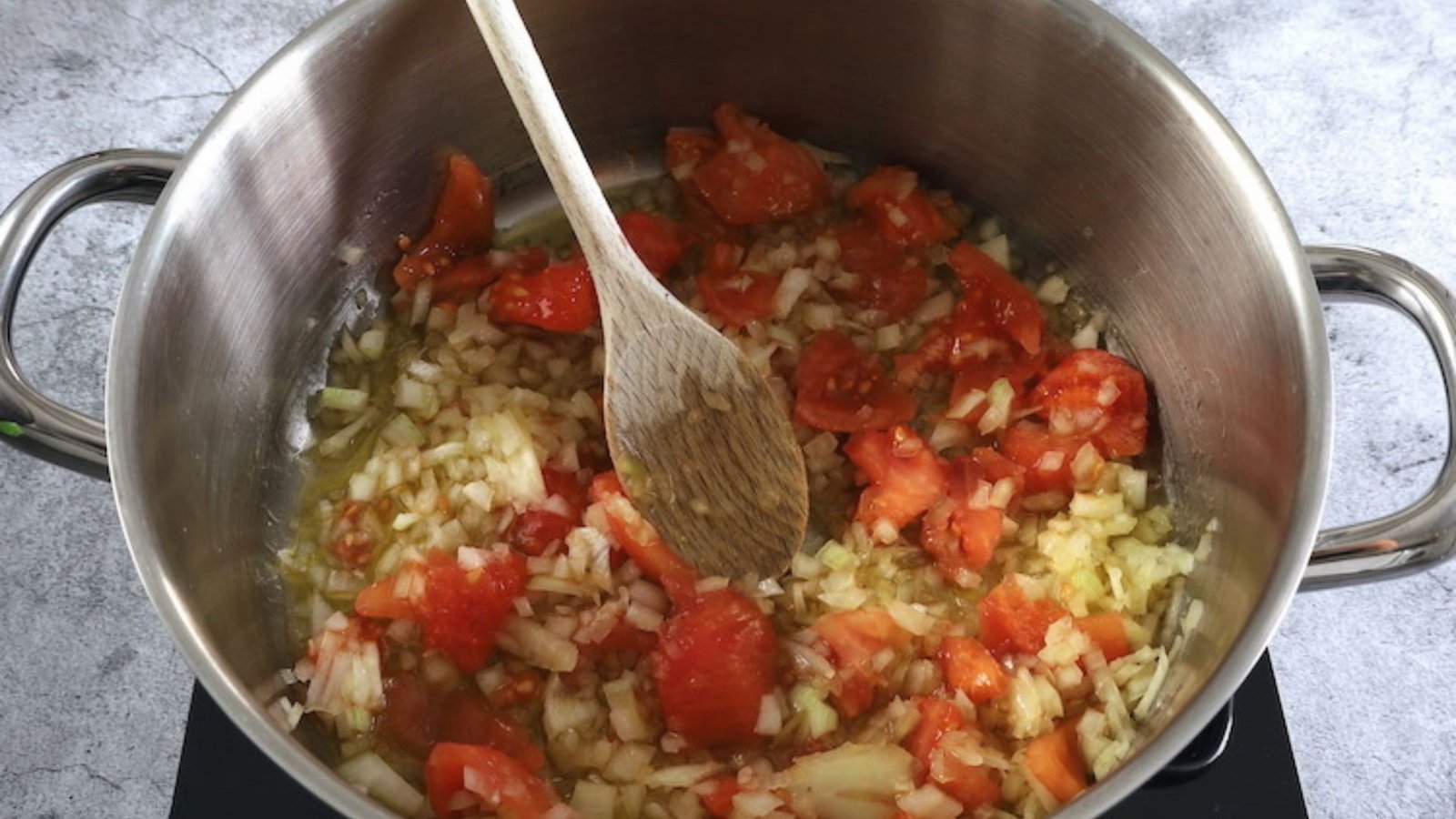 A pan on the stove with tomatoes and onions sautéing, part of the King Ranch Chicken Casserole preparation.