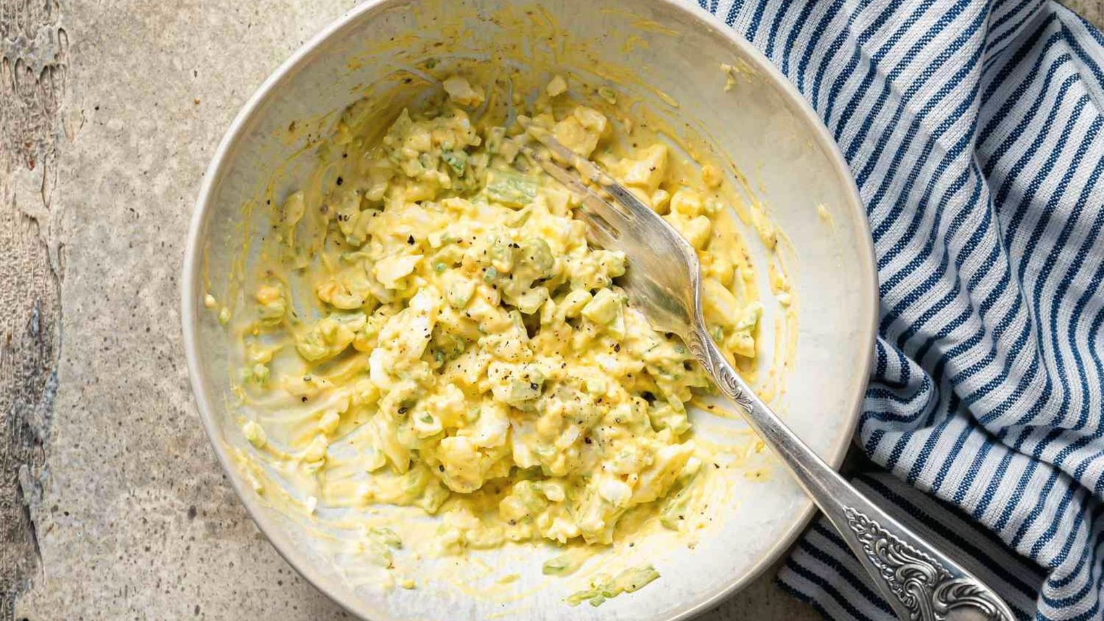 A bowl filled with eggs, pickle and more ingredients in a bowl mixing all together with a spoon.