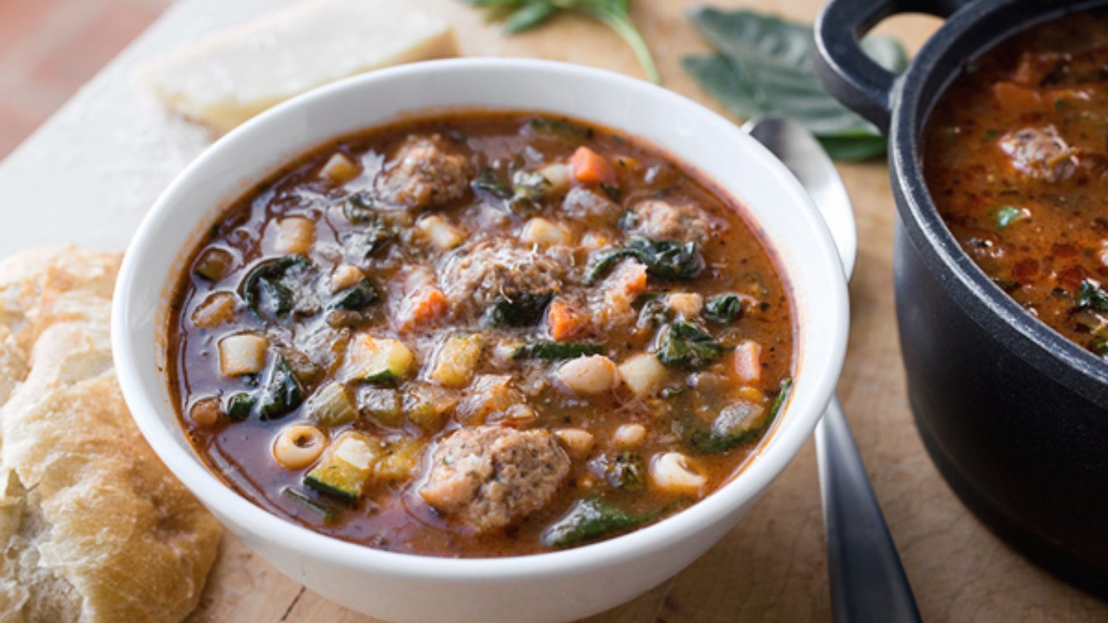 A steaming bowl of minestrone soup featuring meatballs and a variety of fresh vegetables, ready to be enjoyed.