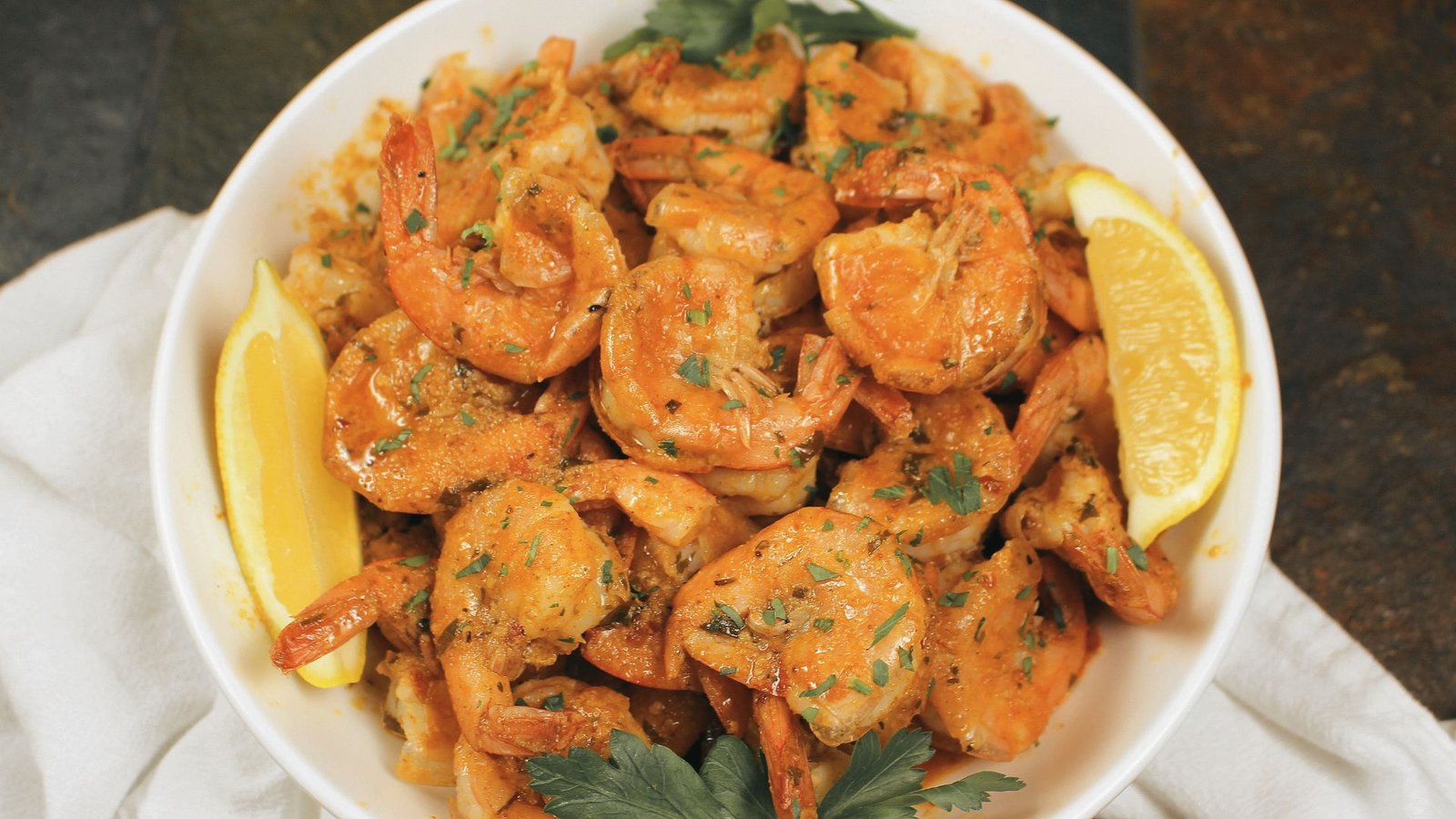 A white bowl brimming with Peel and Eat Shrimp and vibrant lemon wedge.