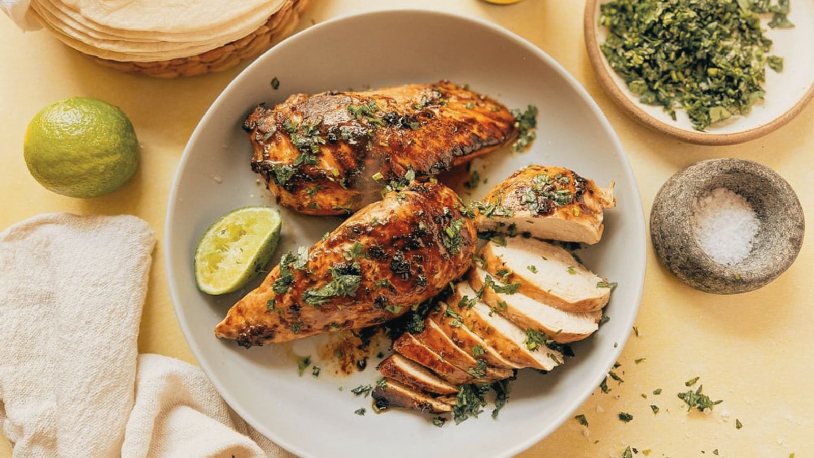 Grilled tequila lime chicken thighs with a charred finish, garnished with fresh lime slices and herbs, served on a plate.