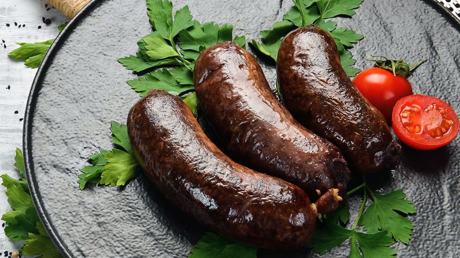 Three homemade deer sausages on a plate, garnished with fresh parsley and cherry tomatoes.