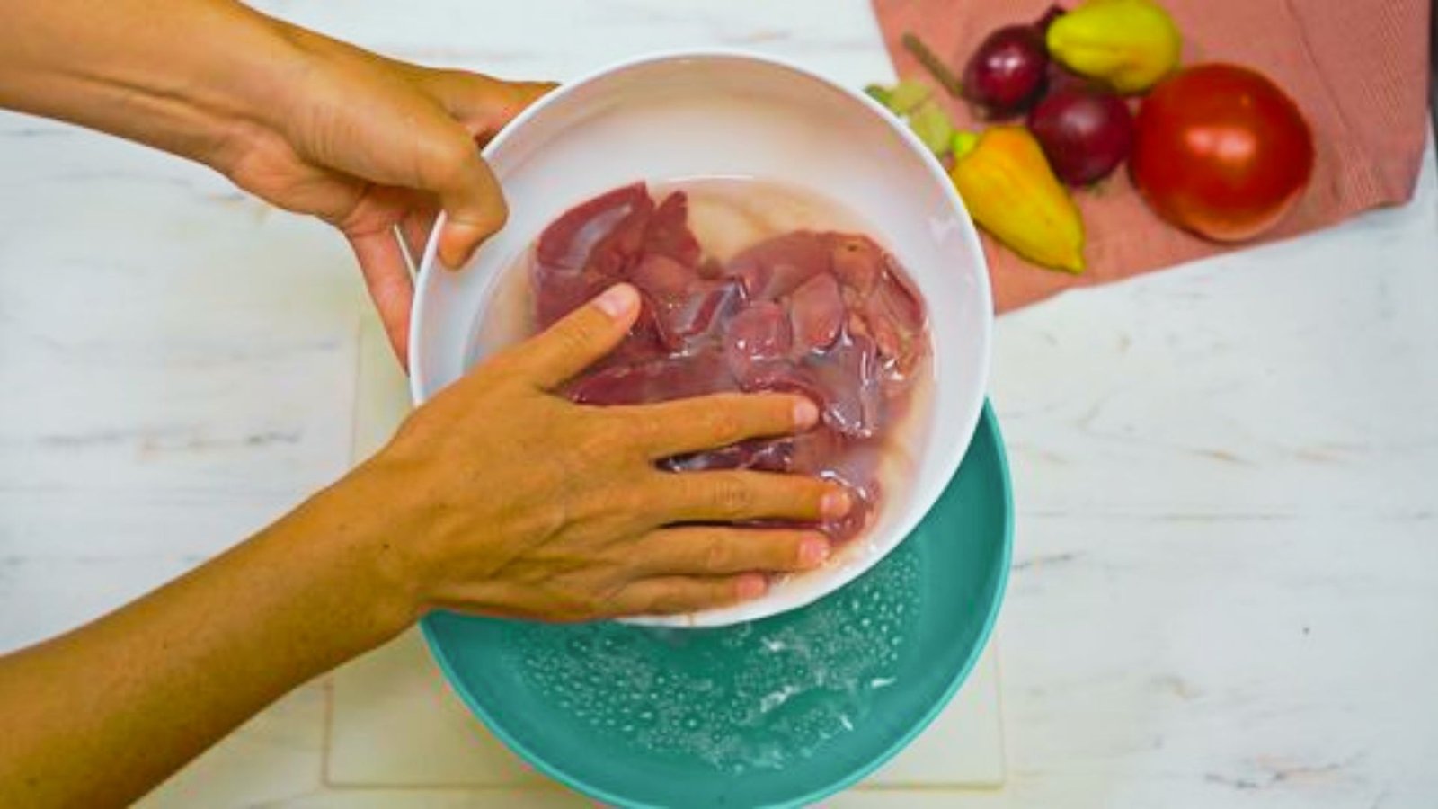 A hand grips a bowl filled with raw livers, ready for rinsing and trimming to ensure even cooking.