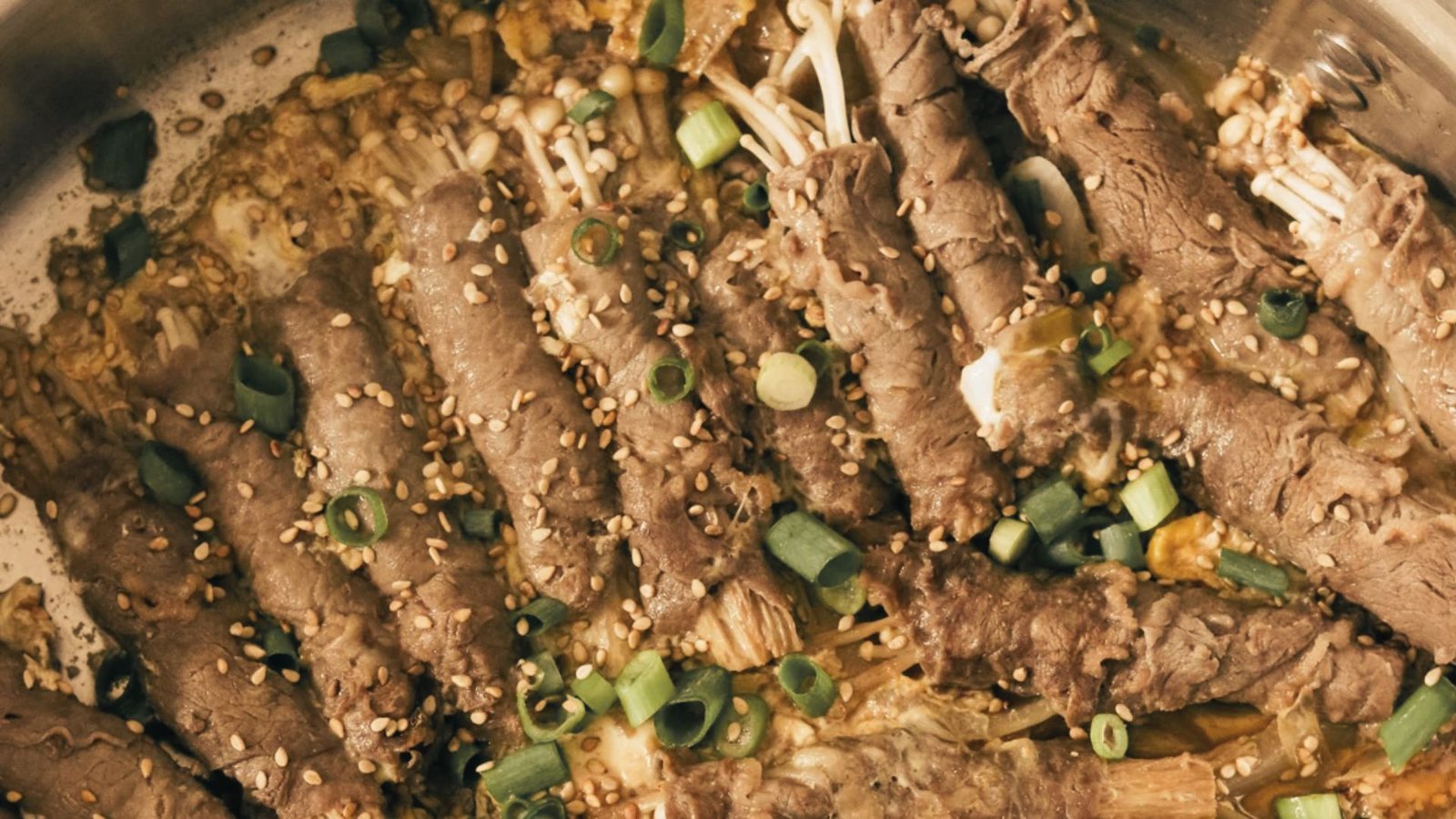 A pan filled with cooked enoki beef rolls, featuring a mix of tender meat and colorful vegetables.