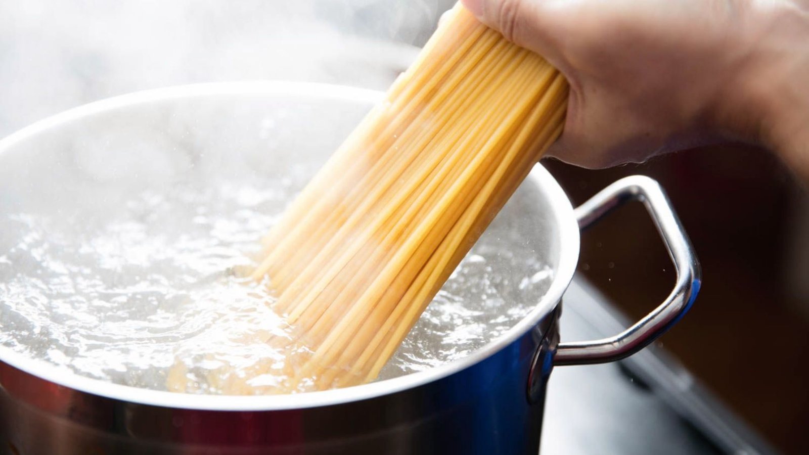 A person stirring pasta spaghetti into a pot of boiling water on a stove, demonstrating the process of cooking pasta.