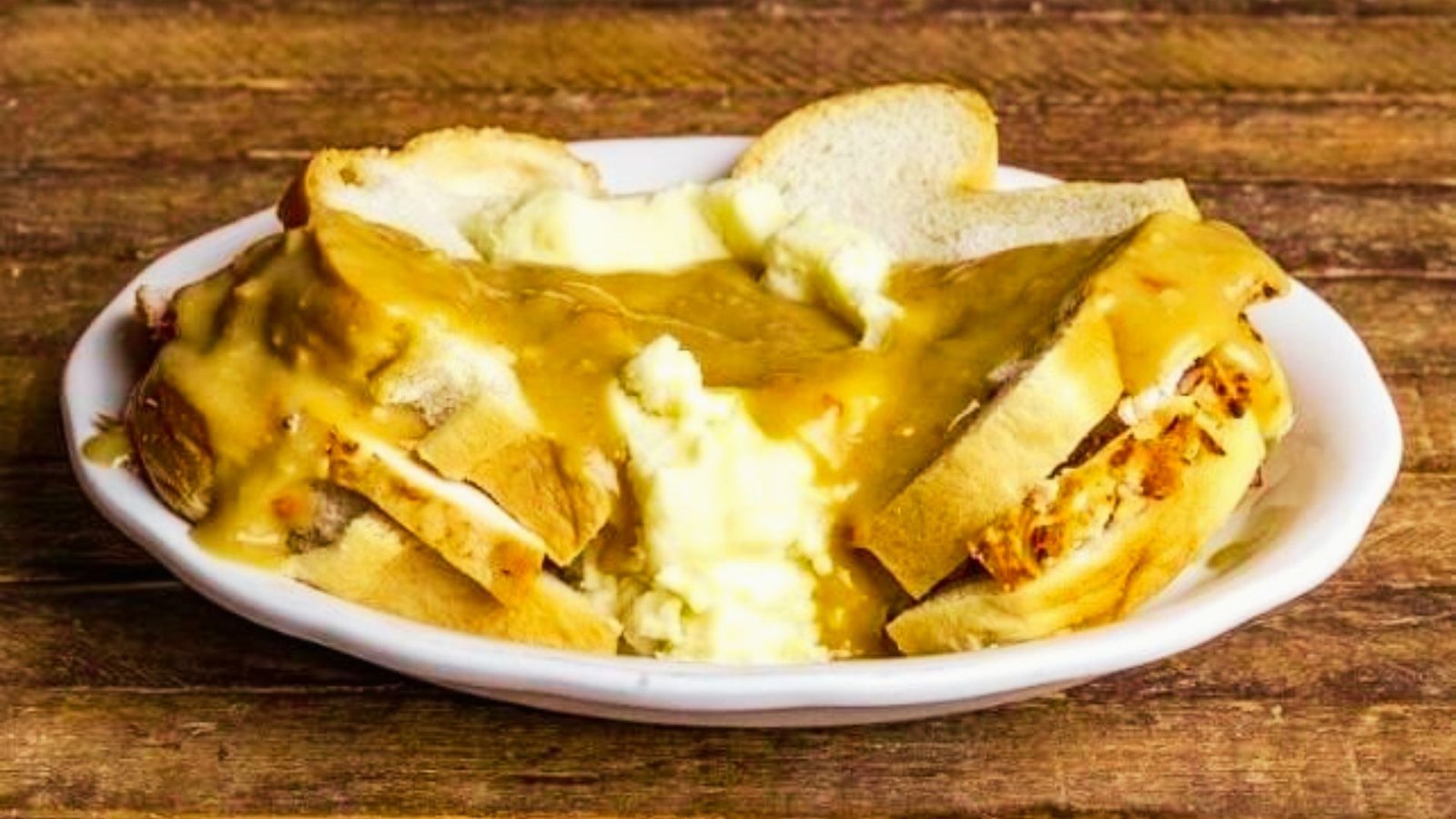 A bowl of Turkey Manhattan with gravy, accompanied by a slice of bread, ready to be served.