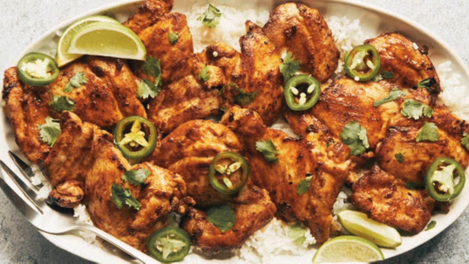 A plate featuring tequila lime chicken thighs, rice, and sliced jalapenos.