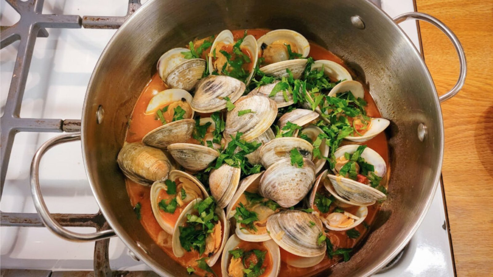 A pot on the stove filled with Little Neck clams and fresh herbs, ready for a white wine and garlic recipe.