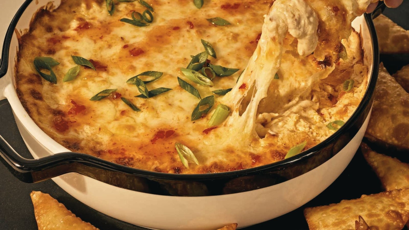 A person dipping bread into a bowl of creamy crab Rangoon dip, illustrating a step in the recipe guide.