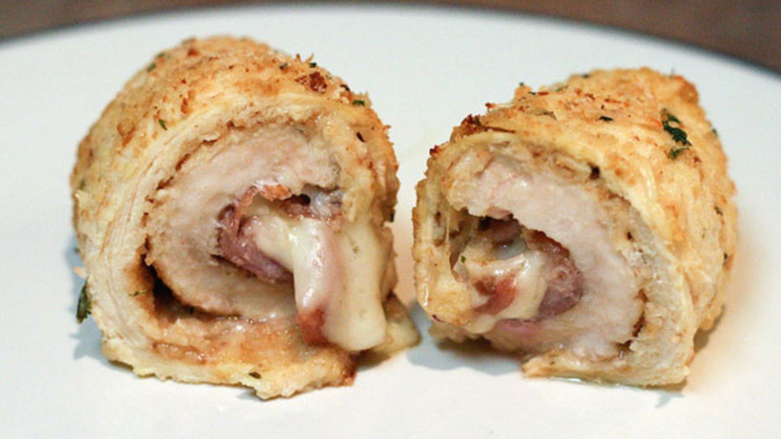 A plate featuring two pieces of chicken rollatini, wrapped in cheese and prosciutto, ready to be enjoyed.