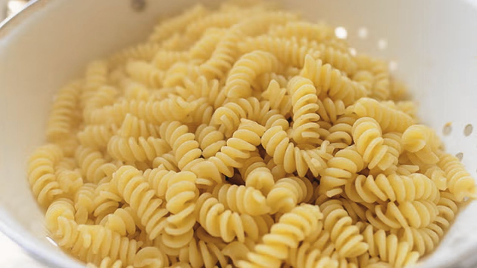 A colander overflowing with pasta, prepared for a shrimp pasta salad.