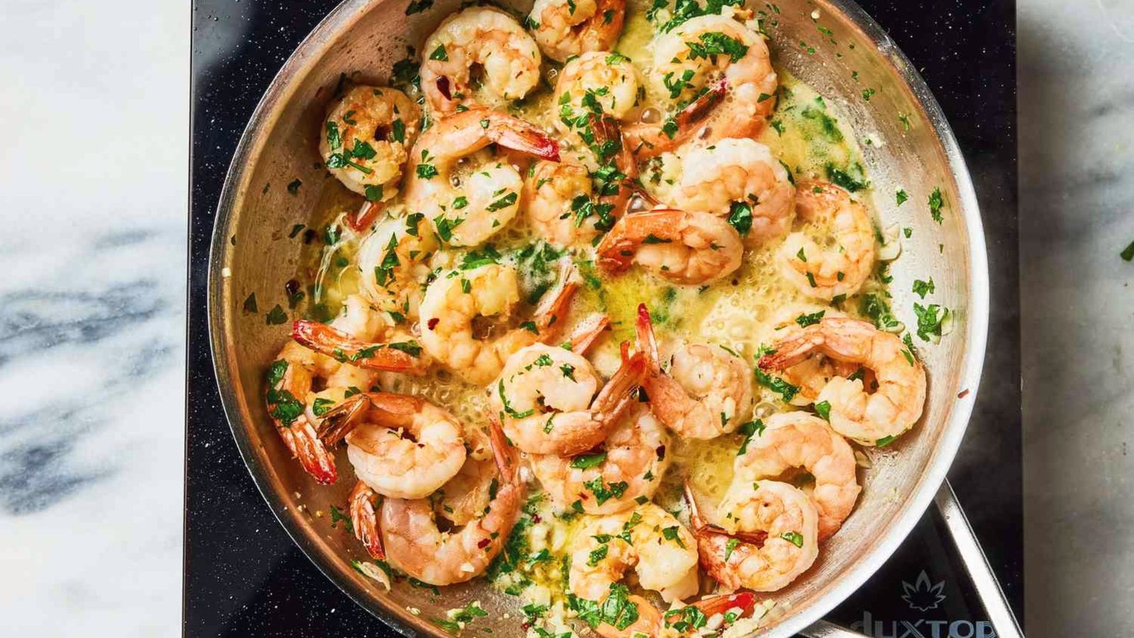 A table displays a pan brimming with shrimp and aromatic herbs, perfect for creating a flavorful sauce.