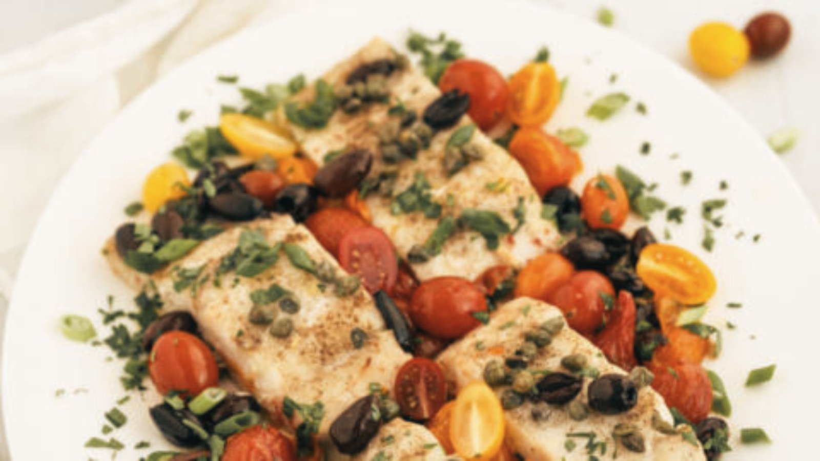 A plate of Mediterranean baked corvina, garnished with grilled tomatoes and olives, highlighting vibrant colors and textures.