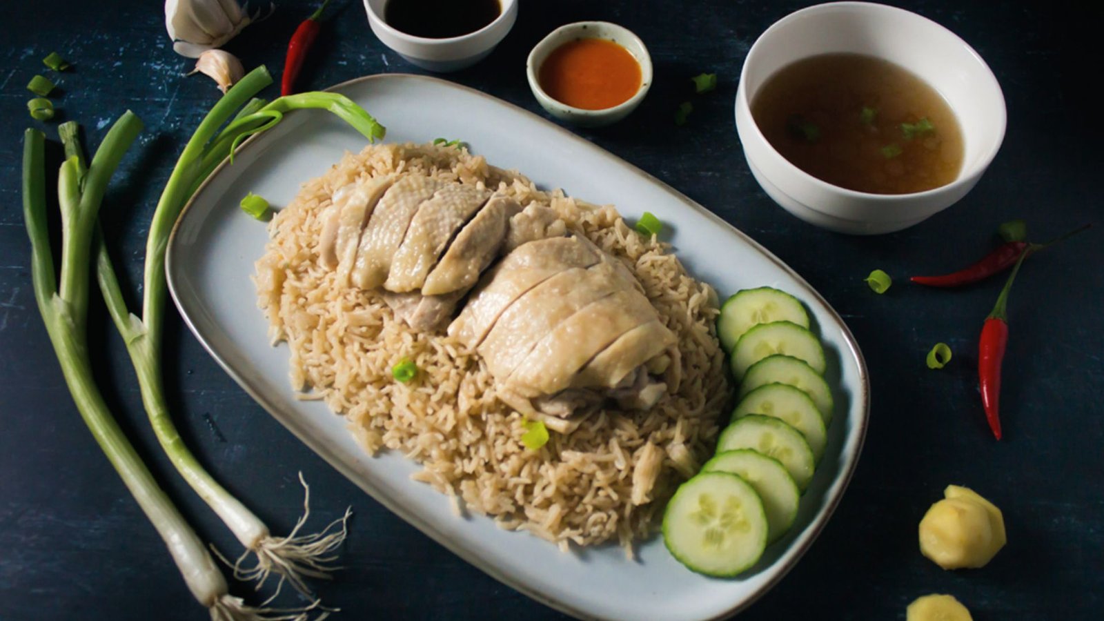 A plate of Hainanese chicken rice garnished with fresh cucumber and green onions, showcasing a traditional dish.
