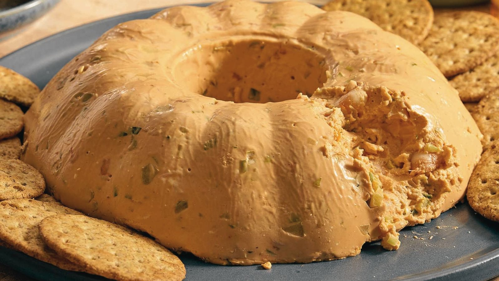 A shrimp mold surrounded by crackers on a plate, featured in a New Orleans-style shrimp mold recipe.