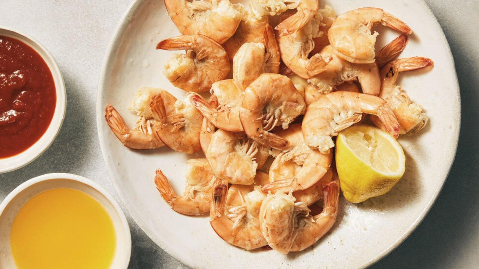 A plate of peel-and-eat shrimp served with a lemon wedge and dipping sauce, showcasing a flavorful seafood dish.