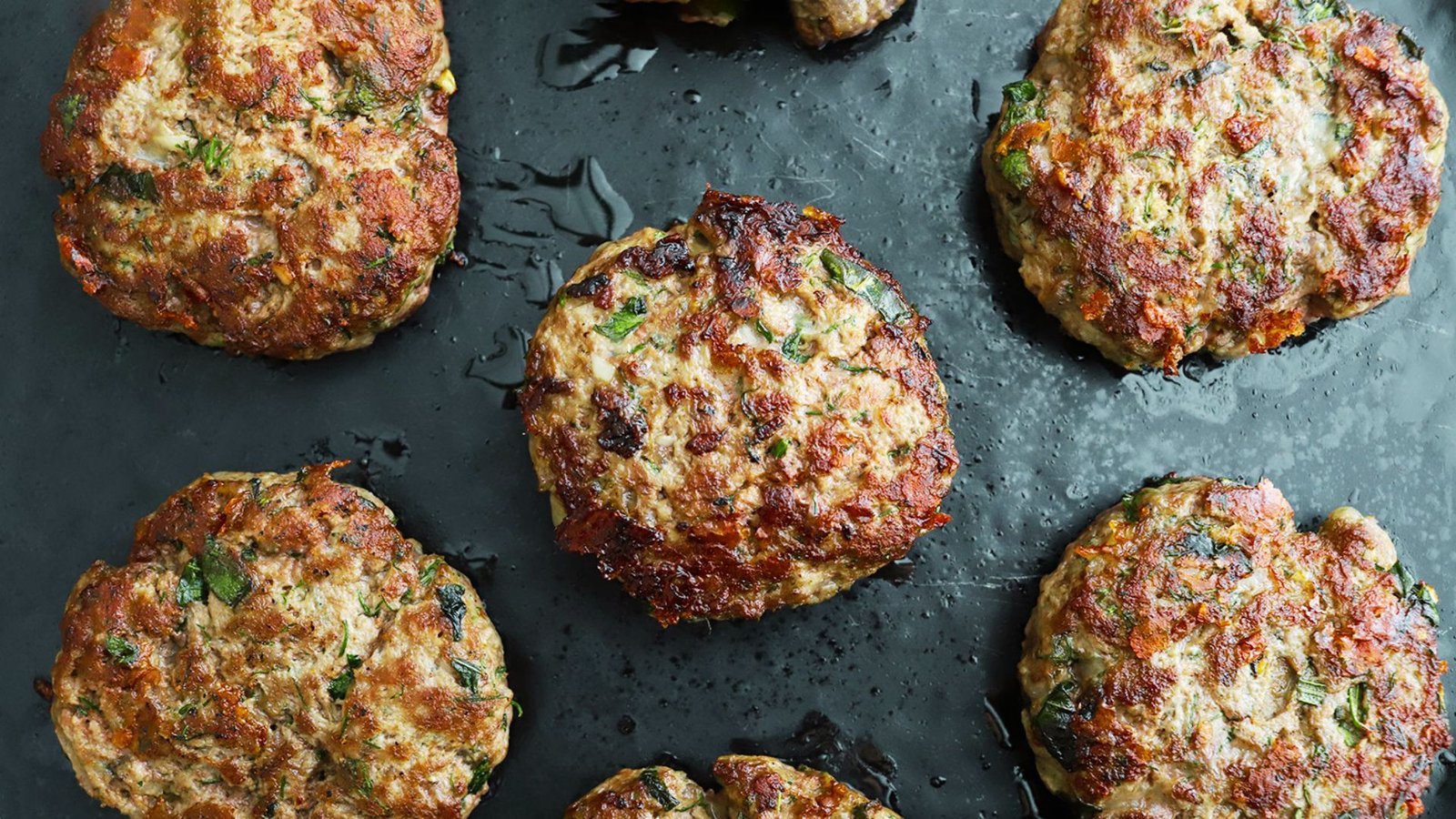 A baking sheet holds six uncooked meat patties, illustrating the process of preparing ground beef for burgers.