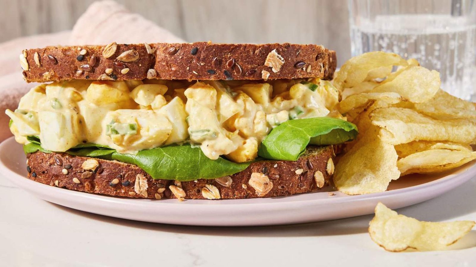 A sandwich filled with egg pickle salad and served with a side of chips, highlighting a delicious meal option.