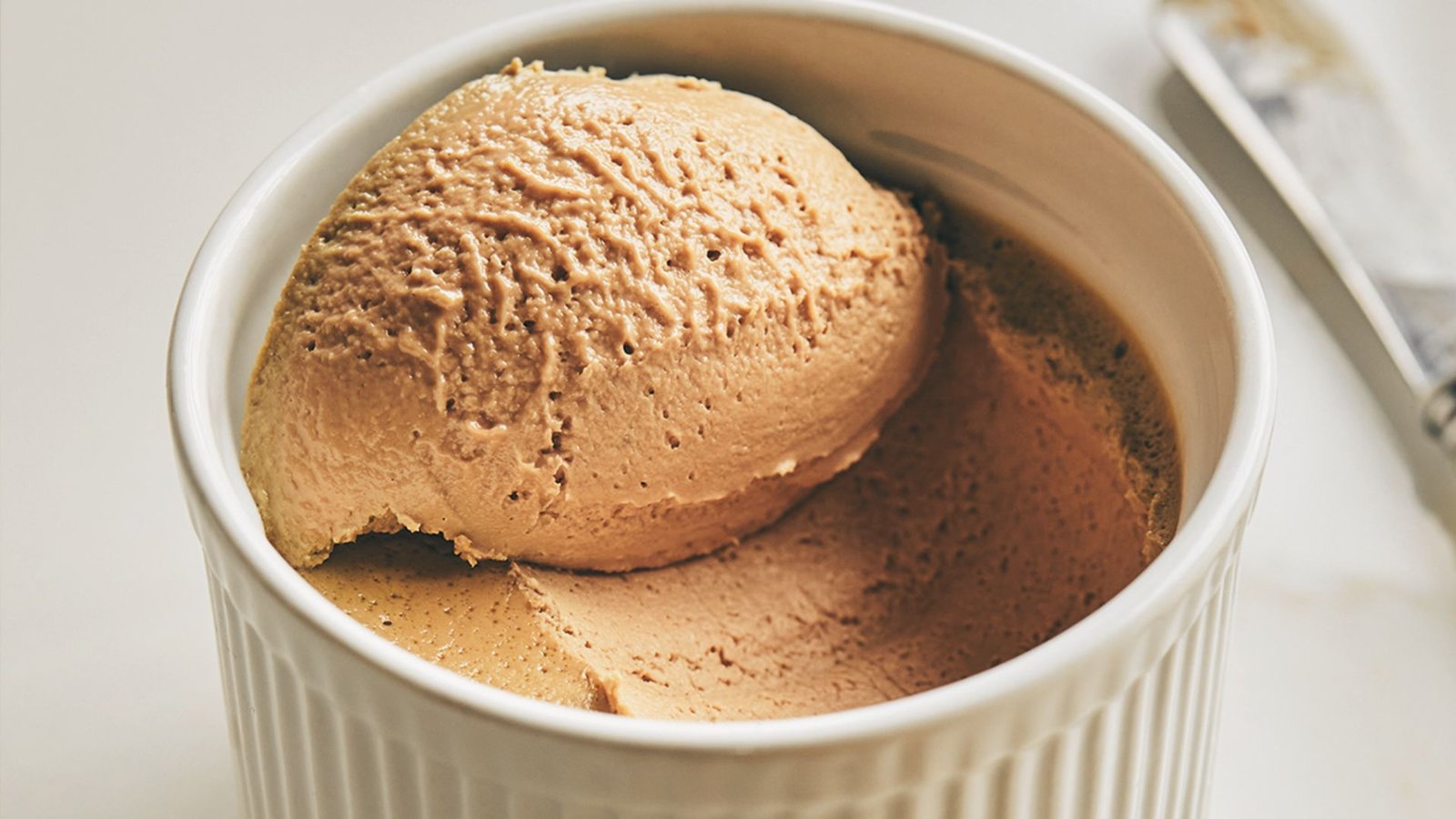 A scoop of Chicken Liver Mousse served in a white cup, indicating a stage in the mousse chilling process.