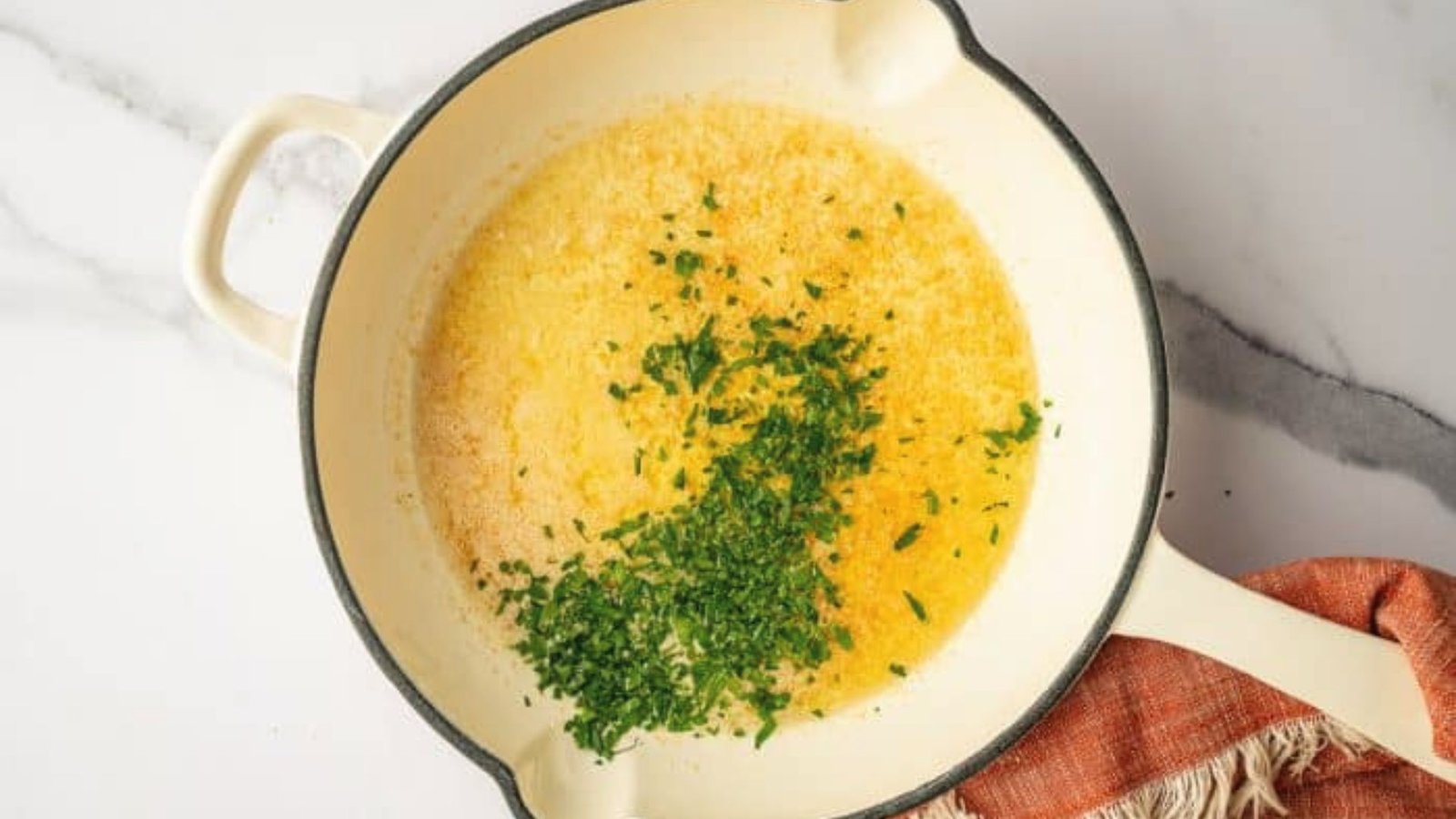 A skillet filled with rich yellow butter sauce, garnished with fresh herbs on top.