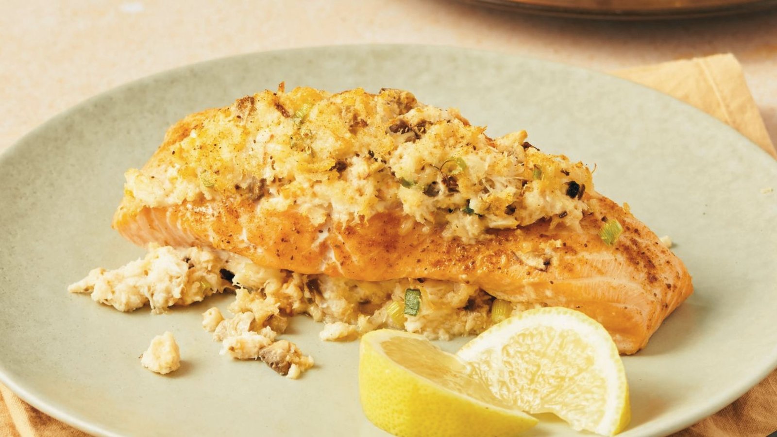 A dish of stuffed salmon filled with crabmeat and shrimp, served with fresh lemon wedges on the side.