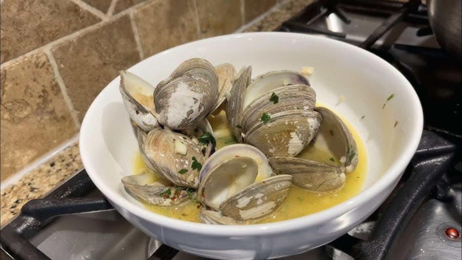 A bowl of clams on a stove top, ready to be steamed with white wine for cooking.