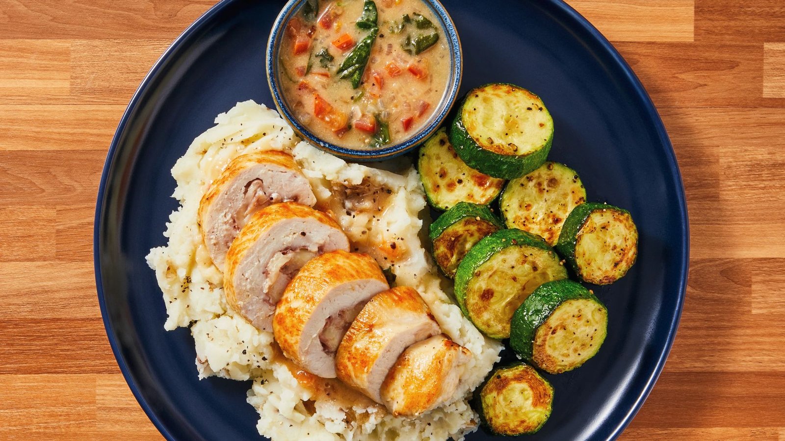 A plate featuring chicken rollatini with prosciutto, served alongside mashed potatoes and sautéed zucchini.
