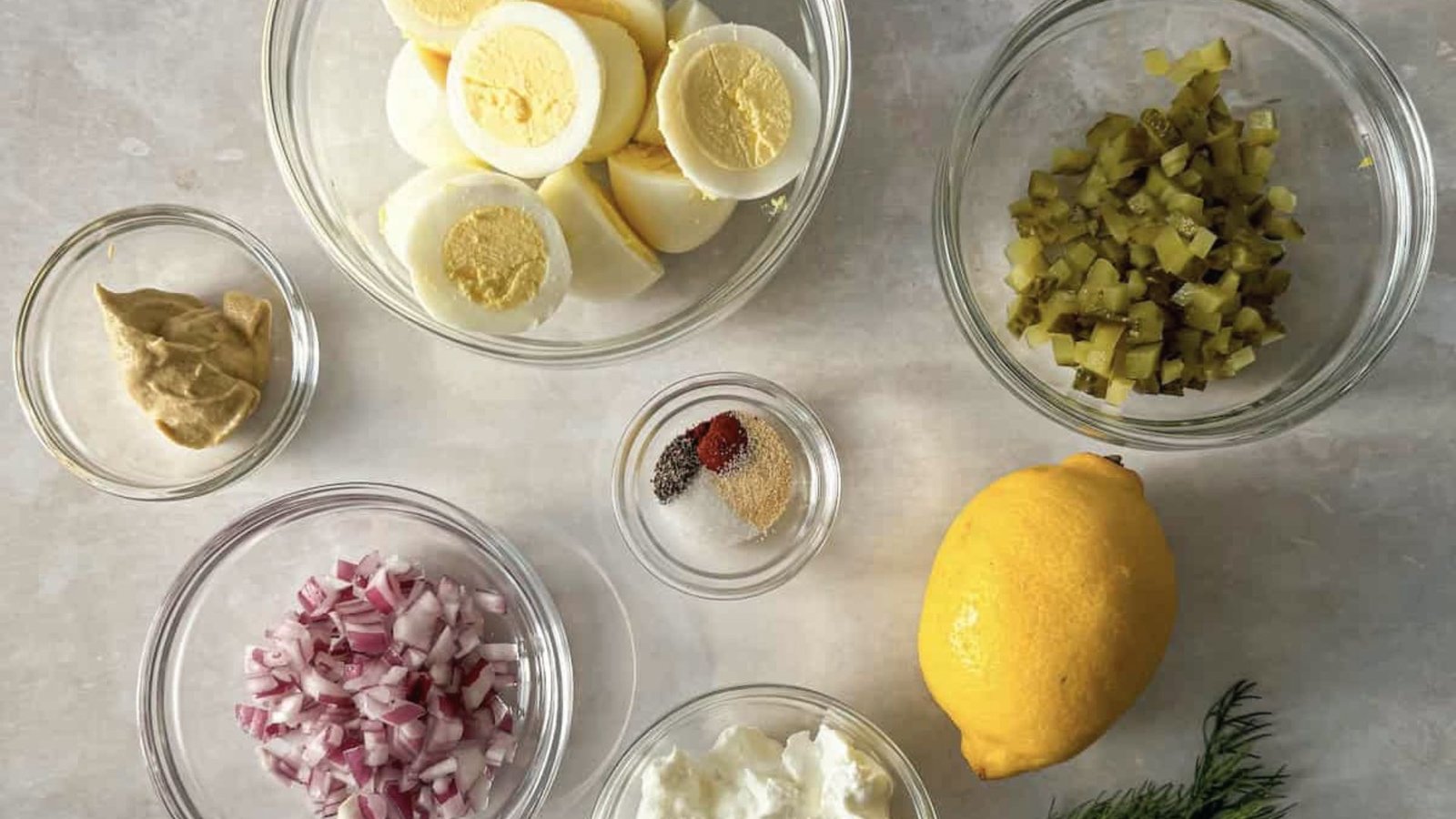 Ingredients for egg salad, including eggs, pickles, mayonnaise, and seasonings, arranged on a kitchen counter.