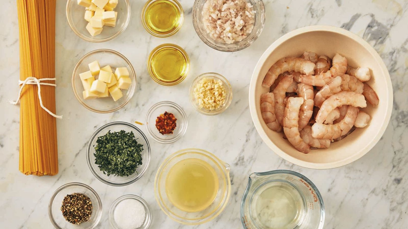 Ingredients for shrimp crab pasta displayed on a marble counter, including shrimp, crab, pasta, garlic, and herbs.