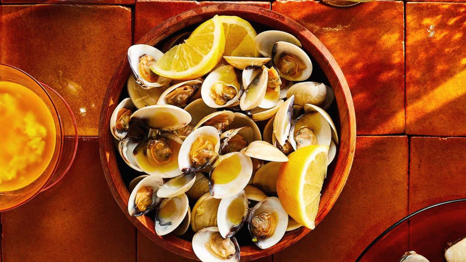 A bowl of clams garnished with lemon and orange slices, finished with fresh herbs for added flavor.