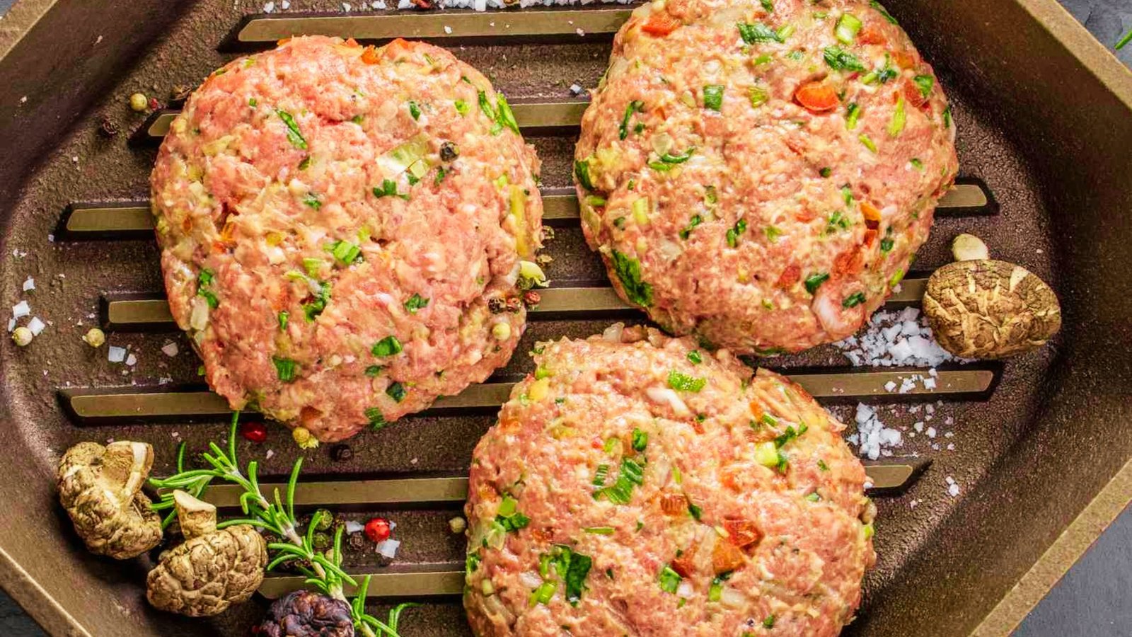 Three ground beef patties are placed on a grill pan, ready to be cooked.