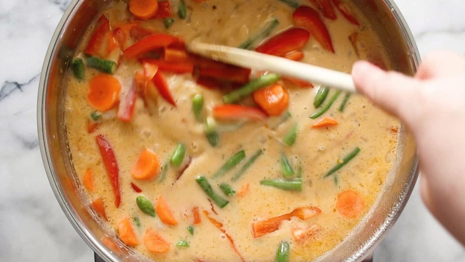 A person stirring a pot of curry with a wooden spoon.