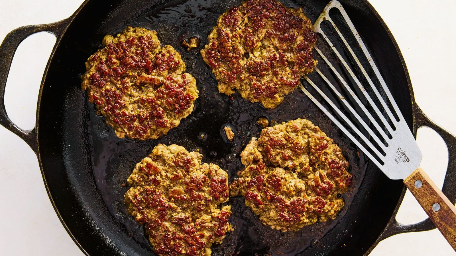 Four patties frying in a skillet, showcasing the process of cooking ground beef for burgers on the stovetop.