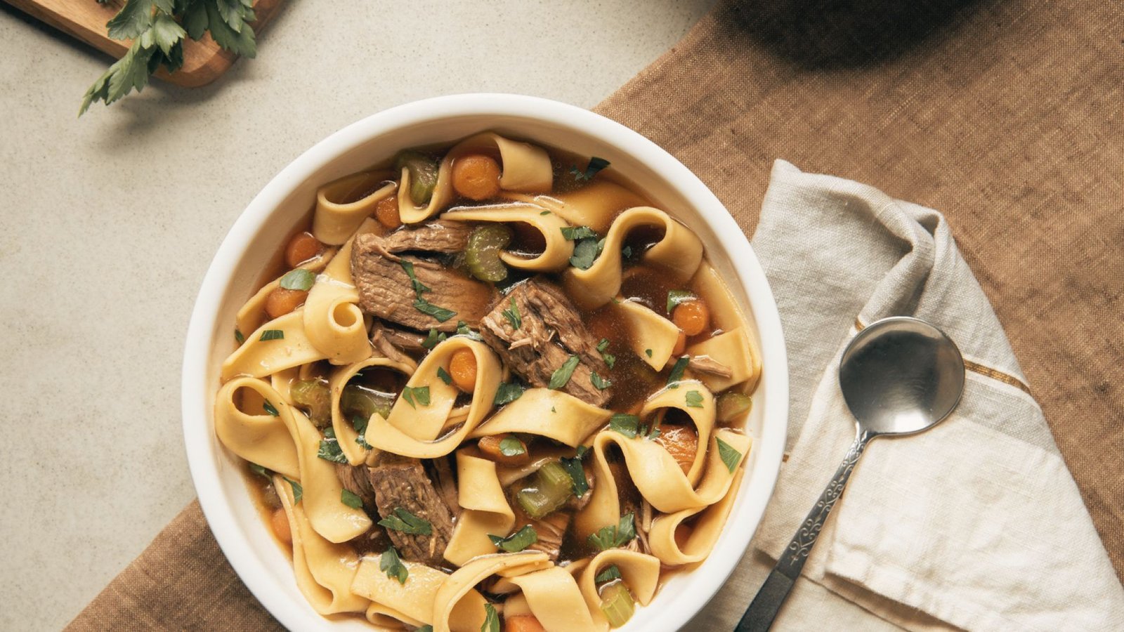 A bowl of beef and Noodle with vegetable stew, showcasing rich beef, carrots, potatoes, and peas in a flavorful sauce.