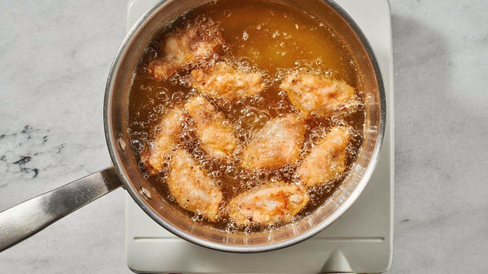 A pan on a stove filled with crispy chicken wings coated in a savory sauce, ready for frying.